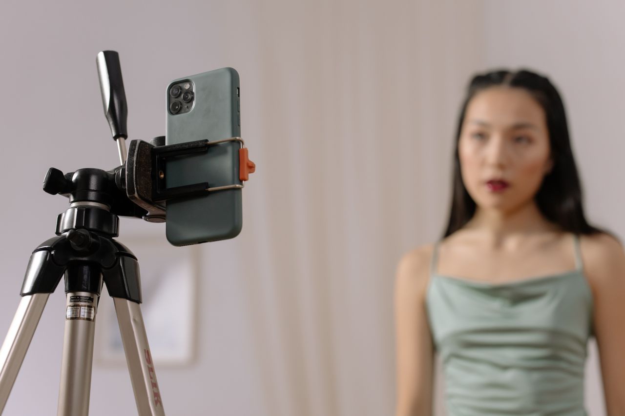 heros-img A woman stands in front of a smartphone set up on a tripod, engaged in vlogging content indoors.
